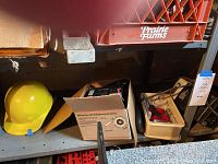 Shelf view showing yellow hardhat on left, Craftsman wet sharpener box in middle, Wen wet stone sharpener in tray on right