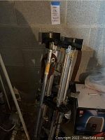 Two pairs of aluminum drywall stilts with adjustable height mechanisms, stacked together in a basement setting.
