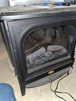 Front view of the electric stove showing the clear glass panel with artificial logs inside.