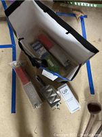 Overview photo showing all items in a black paper bag on a floor including fishing lure molds, pH meter box, and metal ladles.