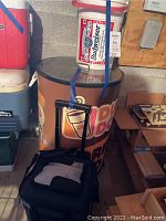 Dunkin Donuts cylindrical cooler with glass top, standing on the floor, next to multiple other coolers and items