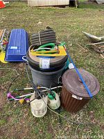 Overview of garden supplies including tubs, coiled hose, spinners, and sprayers on the grass beside a shed.
