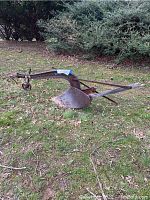 Full view of the rusty metal plow sitting on grass showing frame and curved blade.