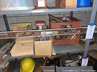 Metal shelving in basement with spirit levels and crate containing masonry spreaders with other tools.
