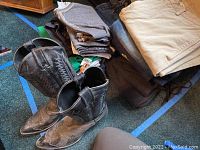 Men's black cowboy boots and folded assorted pants including jeans and sweatpants