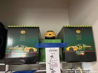 Photo showing two boxed 1/18 scale John Deere precision diecast stock car replicas with a small yellow toy car on top of the green box in the center, boxes display John Deere numbered race cars 23 and 97.