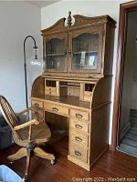 Full view of oak rolltop desk with detachable glass-door hutch and Windsor-style chair on hardwood floor