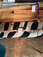 Partially rolled-up rug showing black and white striped pattern with fringe edges, laid next to wood pieces in attic space.