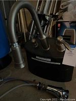 Photo showing Moen Aberdeen faucet with curved spout and single-handle in stainless steel attached to black base of soap dispenser, with plumbing fixture accessory visible on ground.