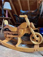 Side angle showing the solid wood motorcycle rocker with detailed handlebars and seat, placed in an attic environment.