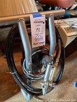Paint sprayer wrapped within its metal frame with attached hoses and spray gun, tagged as lot 197.
