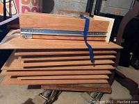 Stack of eight pine cabinet doors with a smooth rectangular design, natural wood, secured with blue strap, small wooden dolly beneath.