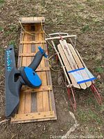 Photo of all three sleds side by side on grass: wooden toboggan, Flexible Flyer sled, and Snow Blade sled with steering blade.