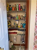 Photo of closet shelving showing an assortment of cleaning supply bottles and sprays such as Lysol, and folded table linens on lower shelves