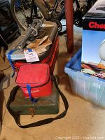 Photo showing green metal toolbox with carrying strap beside a red zippered pouch and cardboard pieces on top.