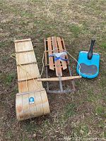 Three winter sleds - wooden toboggan, wooden sled, and blue mini luge on grass