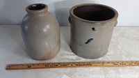 Photo showing the two stoneware crocks side by side with a ruler for scale, indicating the sizes of 2-gallon and 1-gallon respectively, the larger crock featuring two blue decoration marks and typical aged glaze.