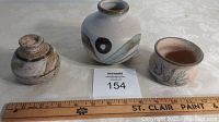 Photo of three art pottery pieces on a white cloth next to a wooden ruler for scale.