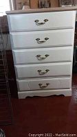 Front view of white wooden chest of drawers with brass handles and paneled drawer fronts