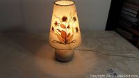 Lit side table lamp showing floral lampshade and pottery base.