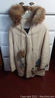 Front view of beige wool ladies coat with fur-trimmed hood and Inuit motif decorations on pockets and cuffs.