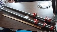 Two long 3/4 x 48 inch metal pipe clamps with red tightening parts placed on a table with a measuring stick.