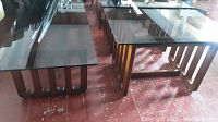 Photo showing four tables—one long rectangular coffee table and three smaller end tables side by side, all with smoked glass tops and wooden bases.