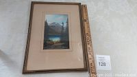 Framed pastel painting of lake and mountain scene with measuring ruler for scale