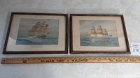 Two framed prints side by side on a table with a wooden ruler measuring them