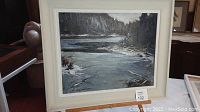 Full view of framed oil painting depicting a late afternoon lake scene with water, trees, and rocky shoreline under overcast light.