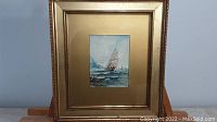 Full view of the framed painting showing the sailboat scene and the gold-tone frame.