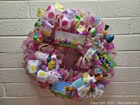 Front view of colorful Easter wreath with mesh, large polka dot bows, and decorative eggs against brick wall.