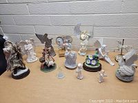 Wide view showing 14 music boxes and figurines including animals, angels, Santa, and children figures arranged on a table against a brick wall.