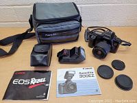 Full setup showing camera, lens, flash, manuals, lens caps, and carrying bag on table.