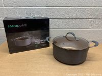 Copper nonstick 5 quart Dutch oven with glass lid shown alongside the original packaging box featuring product name and brand.
