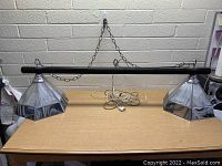 Full view of the hanging billiard light fixture on a wooden table showing the dark wooden beam with two large glass shades on each end plus mounting chains and power cord.