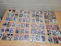 Overhead photo of a large collection of football trading cards featuring Dallas Cowboys players arranged in grid format on a table, including prominent players Troy Aikman, Emmitt Smith, Michael Irvin, and others. Cards are sleeved.