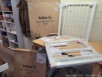 Two boxed Safety 1st Easy Install Walk-Thru baby gates with one gate partially unpacked and wrapped in protective plastic on table.