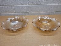 Top view of two amber-colored carnival glass bowls with ruffled edges placed on a flat surface.
