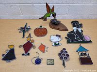 Photo showing a collection of 12 stained glass art items arranged on a table, including animals, seasonal motifs, and abstract shapes.