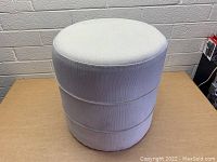 Front view of the light grey cylindrical ottoman showing fabric texture and stitching detail.