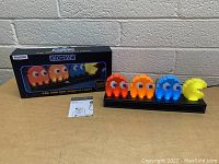 Pac-Man and Ghosts light set with box and paperwork on table in front of brick wall.
