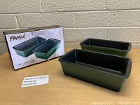 Two rectangular Parini loaf pans shown with product box and safety info card, placed on wooden surface against brick wall background.