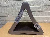 Front and side view of the triangular shaped cardboard cat scratcher with beige frame on a table.