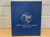 Blue hardcover book with silver embossed United Nations logo and text 'United Nations Flag Stamps - 1980 Series'.