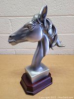 Silver-colored horse bust statue from a left side angle on a wooden base with a beige background.