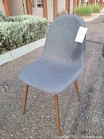Front angle view of the grey upholstered Project 62 dining chair with wood legs outdoors.