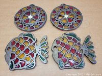 Front view of two round and two fish-shaped vintage stained glass trivets showing colorful glass insets and metal frames.