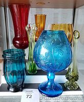 Seven colorful glass art pieces displayed on a shelf, highlighting the variety and colors.