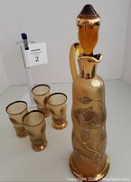 Amber-colored Czech Bohemian glass decanter with gold floral design and four matching glasses.